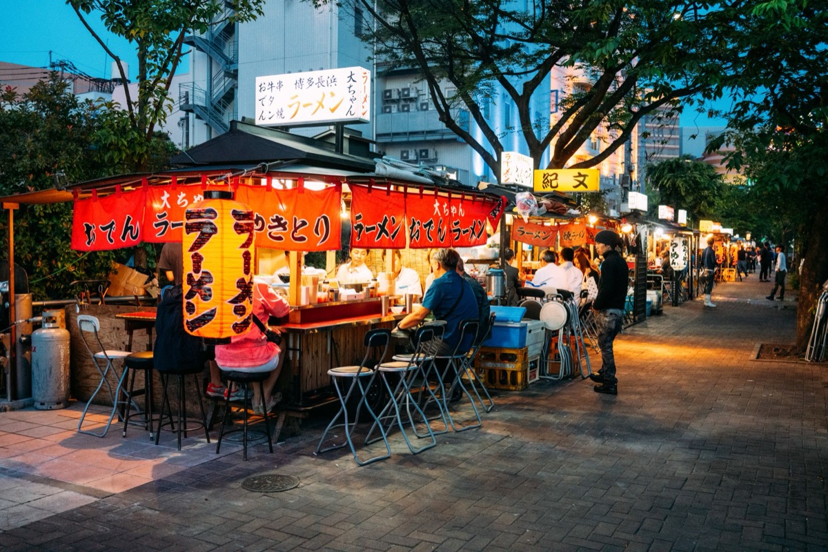 A street vendor in Tokyo selling skewers and rice balls under a bright overhead light