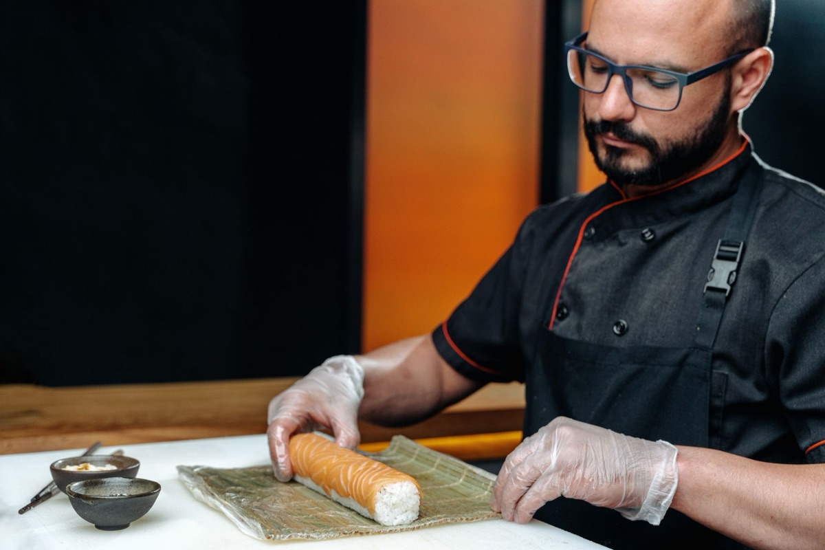 cocinero en uniforme blanco prepara sushi